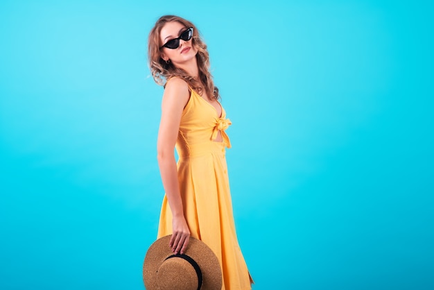 Beautiful European girl with a charming smile, in a fashionable bright yellow dress, sunglasses and a straw hat