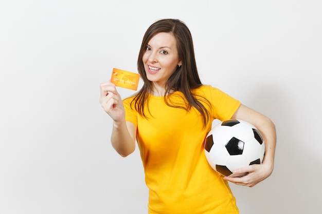 Beautiful European young cheerful woman, football fan or player in yellow uniform holding credit card soccer ball isolated on white background. Sport, play football game, excitement lifestyle concept.