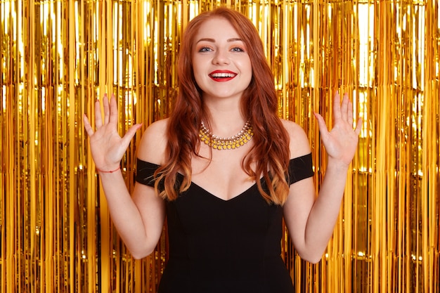 Beautiful excited woman with beautiful red hair at celebration party, birthday or New Year eve celebrating, happy girl in dress raising hands up