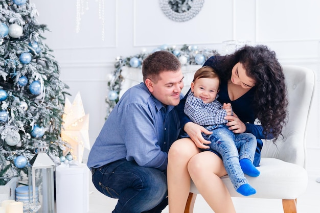 Beautiful family looking into the camera on the background of Christmas tree and fireplace mom with her son sitting on an armchair