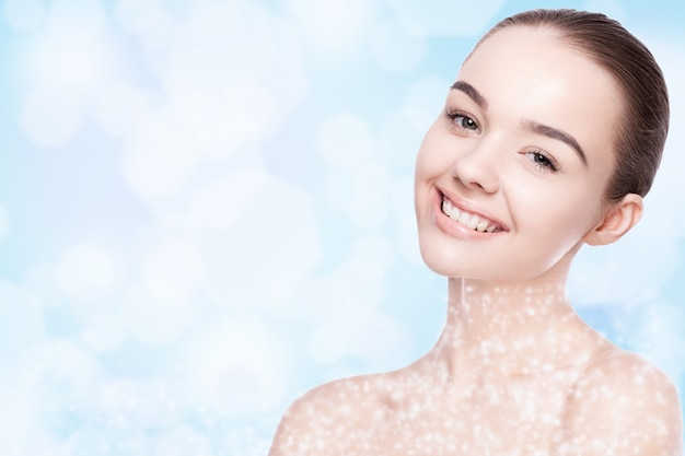 Beautiful fashion model girl with cute smile natural makeup spa skin care portrait on blue bokeh background with shiny glitter stars on neck