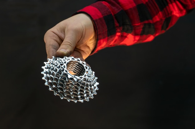 A beautiful fashionable bicycle mechanic in a red plaid shirt holds bicycle parts in his hands Bicycle cassette and mechanic's hands closeup on a black background in a photo studio Bicycle repair