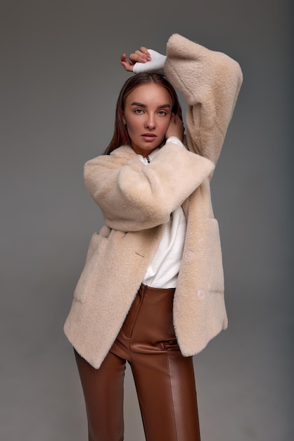 Beautiful fashionable woman in a cozy fur coat on a gray background positive girl posing at the