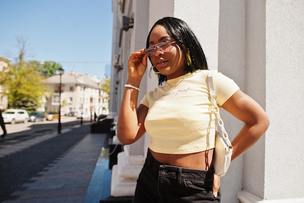 Beautiful fashionable young african american woman posing in street sunglasses yellow top Fashion summer photo Bright colors Nice view afro people