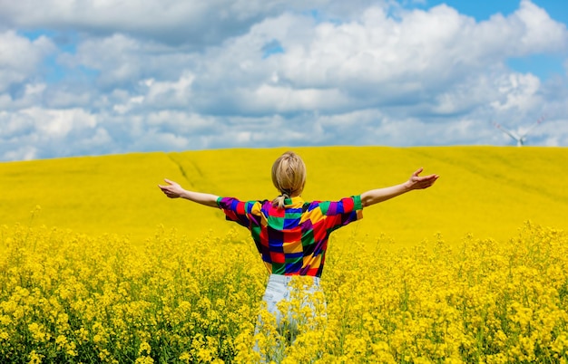 Beautiful female in 90s stylish shirt in rapeseed field