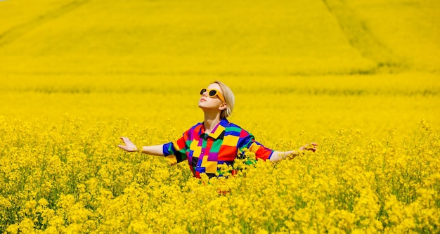 Beautiful female in 90s stylish shirt in rapeseed field