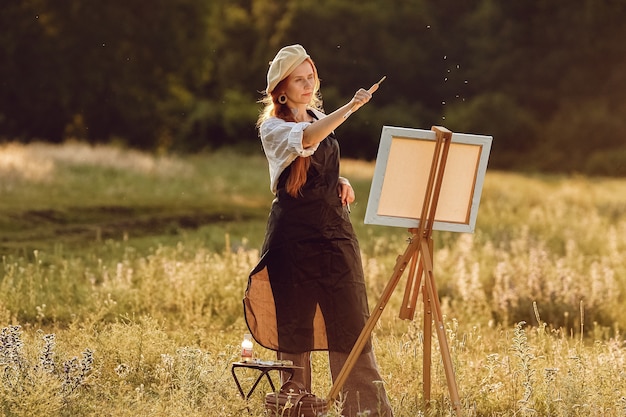 Beautiful female artist painting at sunset in nature