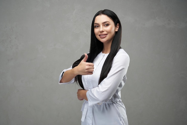 Beautiful female doctor showing thumb up and smiling to camera portrait of pretty brunette woman