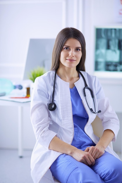 Beautiful female doctor sitting at her working place in a consulting room smiling at the camera