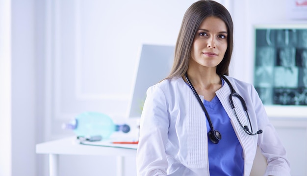 Beautiful female doctor sitting at her working place in a consulting room smiling at the camera