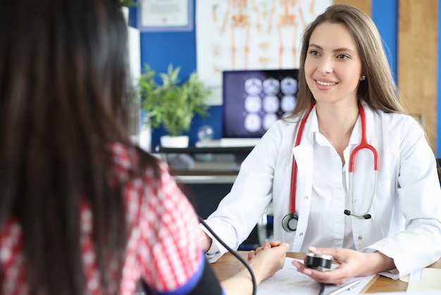 Beautiful female doctor working with patient measures blood pressure