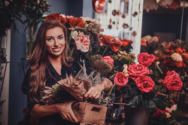 Beautiful female florist is holding decorative box with dried flowers at her own shop.