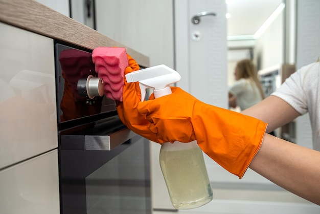 Beautiful female hands in orange mittens wipe the kitchen surface from dust Cleaning concept