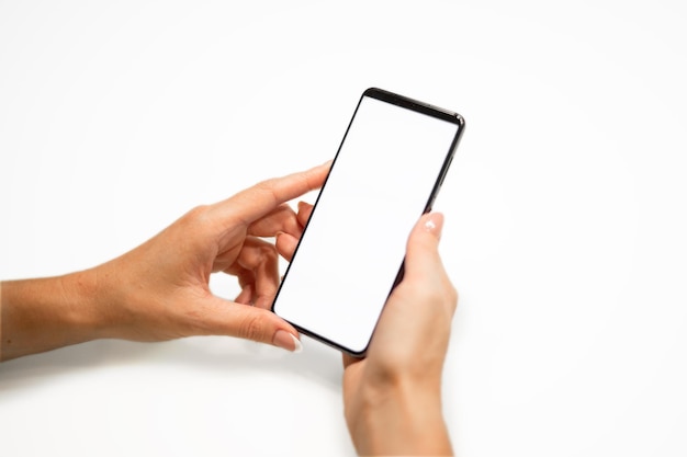 Beautiful female hands with manicure hold a smartphone with a white screen on a yellow background