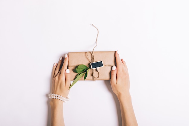 Beautiful female hands with manicure holding a box with a gift on white table