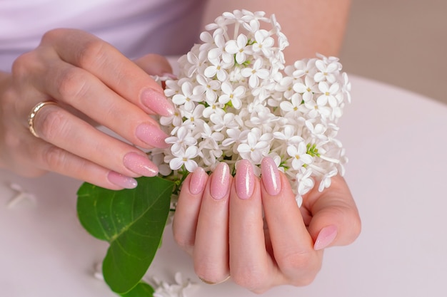 Beautiful female hands with manicure nails pink gel polish and white flowers