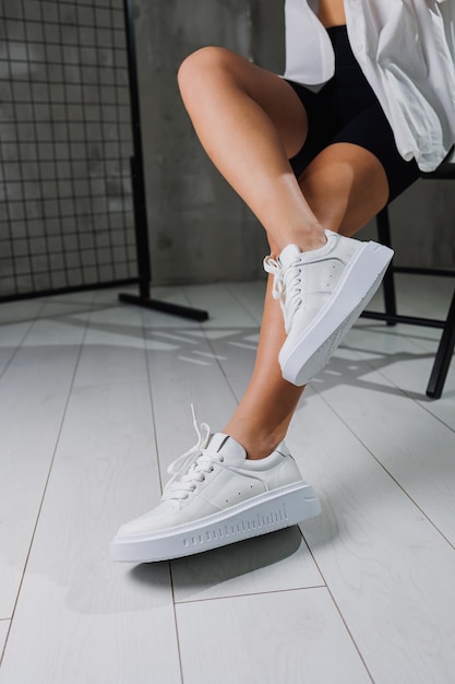 Beautiful female legs in leather white casual sneakers Women's legs with fashionable shoes Casual white women's shoes