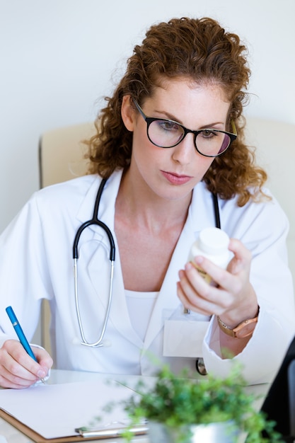 Beautiful female pharmacist holding jar of pills in hands in the office.