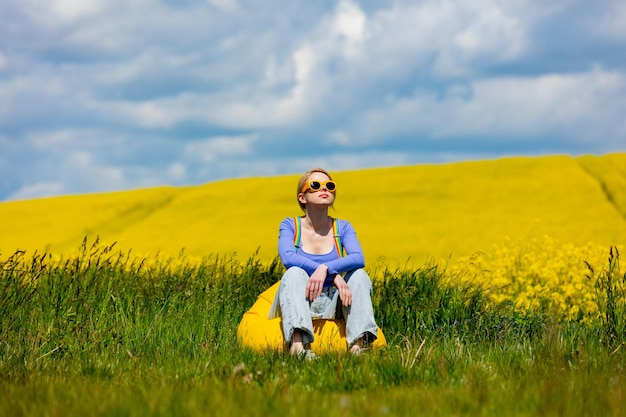 Beautiful female in rainbow LGBT suspenders for pants sitting in bean chair in rapeseed field