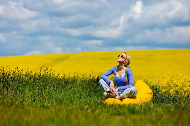 Beautiful female in rainbow LGBT suspenders for pants sitting in bean chair in rapeseed field