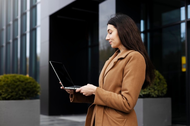 Beautiful female standing outdoors using laptop Young girl working on street checking mail