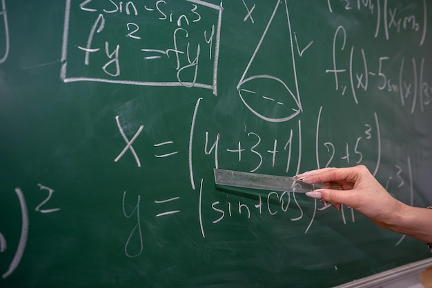 Beautiful female teacher near blackboard learn mathematical in classroom, back view