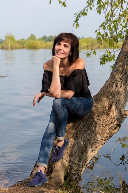 A beautiful female tourist is resting sitting on a tree near the river