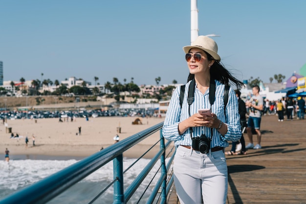 a beautiful female traveler walking nearby the beach and watching beautiful views with her phone on her hand