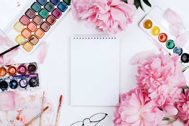 Photo beautiful feminine flatlay mockup with notebook, stationery supplies, watercolors and pink peonies on white