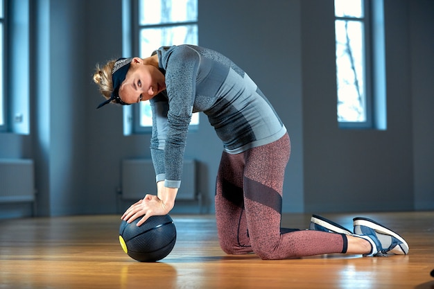 Beautiful fit woman in sportswear posing while sitting on the floor with fitness ball in front of window at gym Healthy girl lifestyle and sport concept