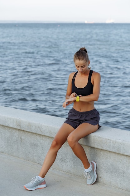 Beautiful fitness girl with a sports watch sitting by the sea