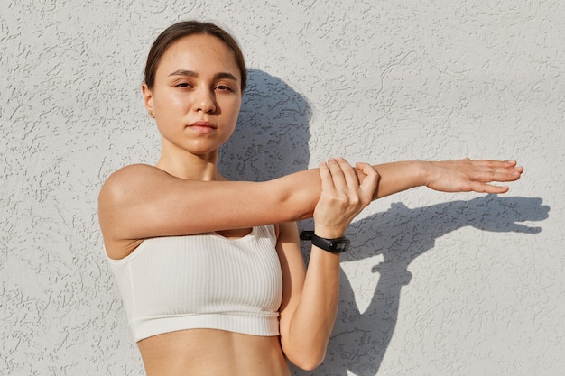 Photo beautiful fitness model girl wearing sport clothes posing against gray wall outdoor, warming up before work out