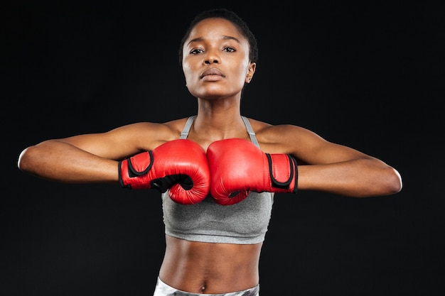 Beautiful fitness woman posing with boxing gloves on black wall