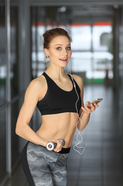 Beautiful fitness woman standing with dumbbell and the telephone