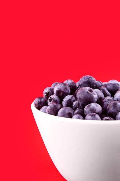 Beautiful fresh blueberries in a white bowl on a red backgroundxAVegan and vegetarian concept