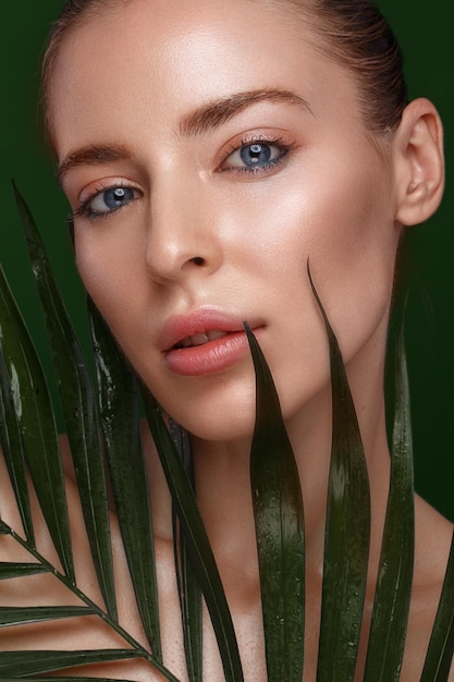 Beautiful fresh girl with perfect skin natural makeup and green leaves Beauty face