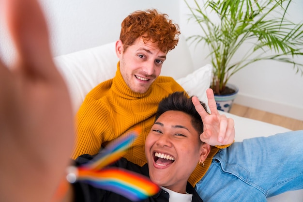 Beautiful gay couple being romantic indoors at home on the sofa gay couple taking selfie and making victory sign lgbt concept