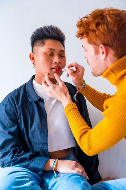 Beautiful gay couple putting on makeup painting their lips being romantic indoors at home lgbt concept