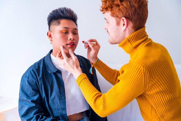 Beautiful gay couple putting on makeup painting their lips being romantic indoors at home lgbt concept