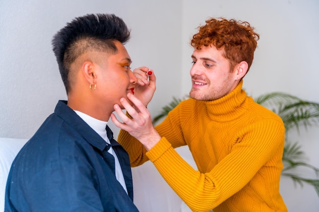 Beautiful gay couple putting on makeup painting their lips being romantic indoors at home lgbt concept