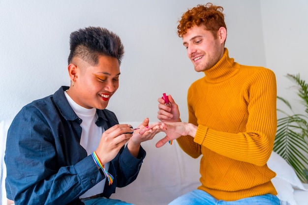 Beautiful gay couple putting on makeup painting their nails and smiling being romantic indoors at home lgbt concept