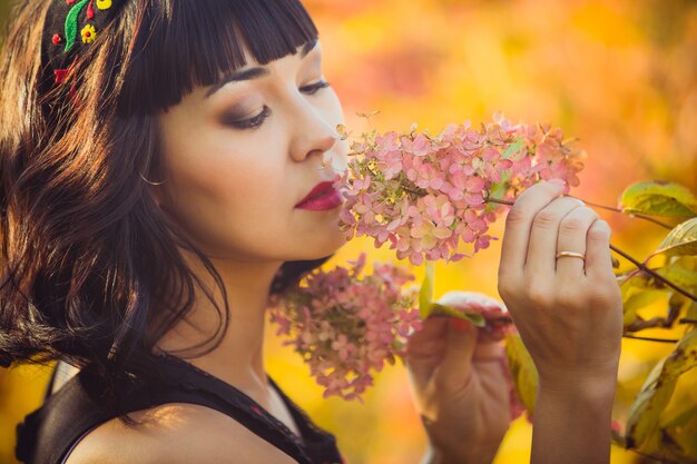 Beautiful girl of Asian appearance in the autumn in the Park smelling flowers