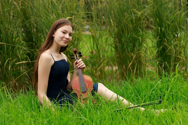 Beautiful girl of Asian appearance with a violin in the park. High quality photo