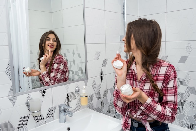 Beautiful girl in the bathroom applies cream on her face. beauty concept.