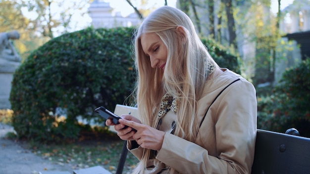 Beautiful girl on a bench in your phone looking photos. Cool autumn park. Soft sunlight