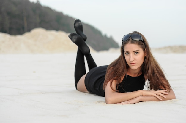 Beautiful girl in a black dress on the beach. Fashion portrait of tanned woman on sea beach