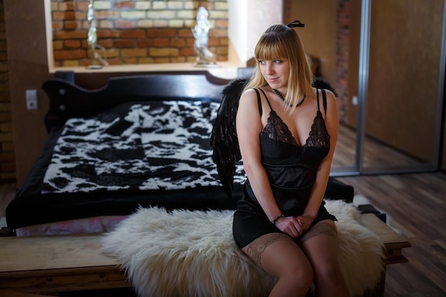 Beautiful girl in black lingerie with black angel wings in a loft interior