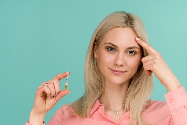 A beautiful girl blogger shows a finger at her face and holds an ampoule