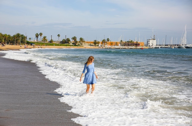 Beautiful girl in blue dress is walking on the beach Amazing summer photo Woman dancing and jumping near the sea Happy and fun emotions Holiday travel concept Slim legs Warm ocean water