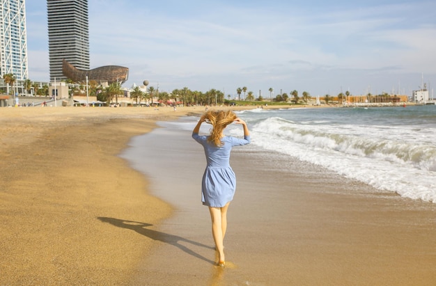 Beautiful girl in blue dress is walking on the beach Amazing summer photo Woman near the sea Happy and fun emotions Holiday travel concept Slim legs Warm ocean water